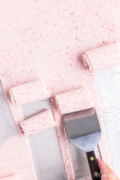 someone using a spatula to cut out pink paper squares