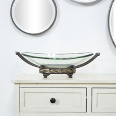 three mirrors on the wall above a white dresser with a glass bowl and metal handles