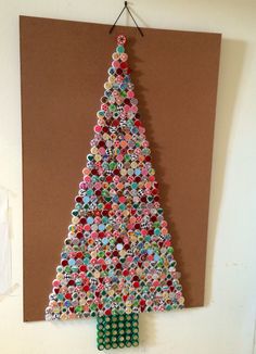 a christmas tree made out of buttons is hanging on the wall next to a piece of cardboard