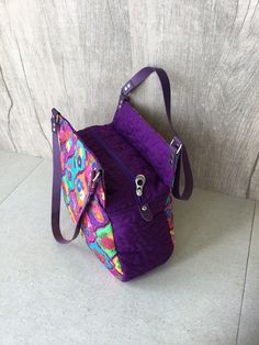 a purple purse sitting on top of a white floor next to a wall with graffiti