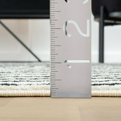 a ruler on the floor with a black chair in the back ground and a white rug behind it