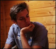 a man sitting in front of a wooden wall with his chin resting on his hand