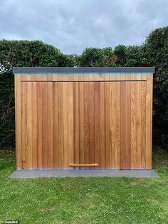 a wooden shed sitting on top of a lush green field next to a hedge covered in grass