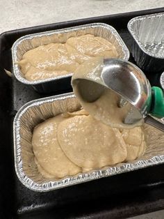 a person pouring batter into tins on top of a baking sheet with other pans in the background