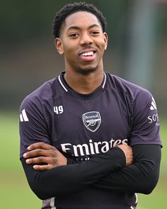 a man with his arms crossed standing in front of a soccer field