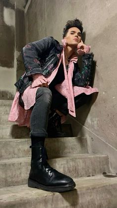 a person sitting on some stairs wearing black boots and a pink coat with an overcoat