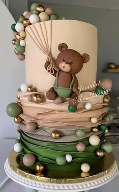 a three tiered cake with a teddy bear on the top and balloons around it