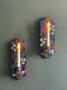 two wall sconces with lit candles on them against a gray wall, decorated with flowers and leaves