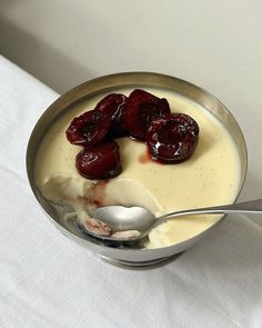 a spoon with yogurt and cherries in it on a white table cloth