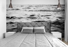 black and white photo of a bed with two lamps hanging over it, in front of the ocean