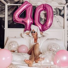 a woman sitting on top of a bed in front of pink balloons and the number forty