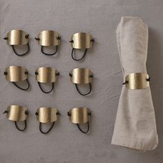 eight brass - plated hooks hang on the wall next to a white linen bag