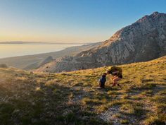 two people are hiking up a hill with mountains in the background and water on the other side