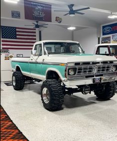 two trucks are parked in a showroom with american flags on the wall behind them