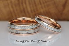 two wedding bands with white and gold inlays are on top of each other