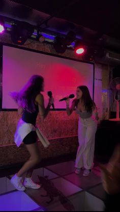 two women singing into microphones in front of a screen