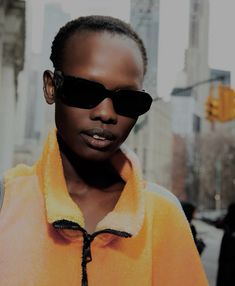 a woman with sunglasses on her head and an orange jacket over her shoulders standing in front of a city street