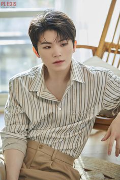 a young man sitting on top of a wooden chair wearing a striped shirt and khaki pants