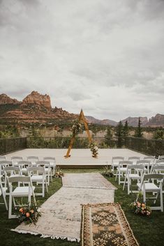 an outdoor ceremony setup with white chairs and flowers on the aisle, in front of mountains