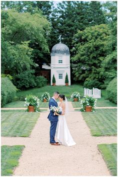 a bride and groom standing in front of a large white house with lots of greenery