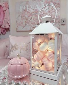 a white lantern with pink ornaments on it sitting on a table in front of pillows