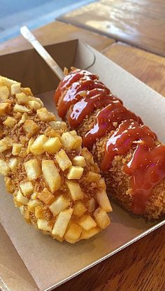 two hotdogs with ketchup and french fries in a box on a table