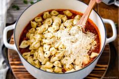 a pot filled with pasta and sauce on top of a wooden cutting board