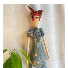 a doll is wearing a blue dress next to a green plant on a white background