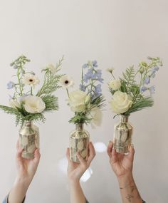 three people holding up vases with flowers in them, one is filled with money