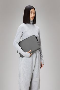 a woman wearing grey sweatpants and holding a gray laptop bag in front of her