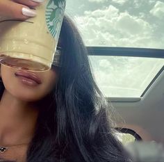 a woman holding a starbucks cup up to her face while sitting in the back seat of a car