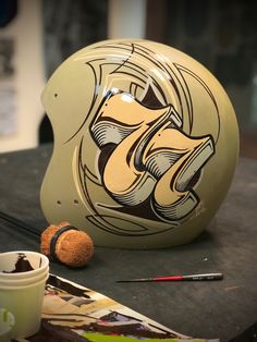 a helmet sitting on top of a table next to a cup and paintbrushes