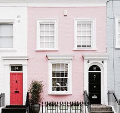 a pink house with white trim and red door in the front, next to a black fence