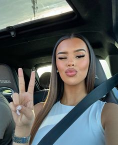 a woman sitting in a car making the peace sign