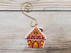 a beaded house ornament hanging on a wooden surface with a metal hook