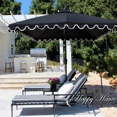 an umbrella and two lounge chairs in front of a white house with outdoor dining area