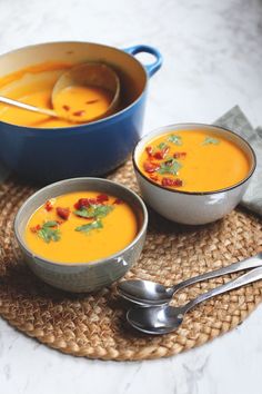 two bowls of soup on a placemat with spoons