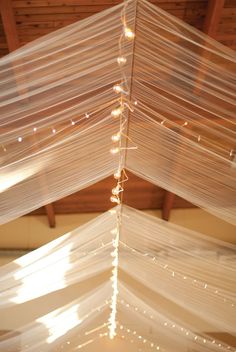 the ceiling is covered with white drapes and string lights hanging from it's rafters