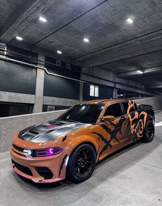 an orange and black car parked in a parking garage next to a wall with graffiti on it