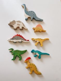 six wooden dinosaur magnets are arranged on a white surface, each with different shapes and sizes