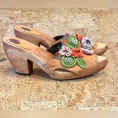 a pair of wooden shoes with crocheted flowers and buttons on the soles