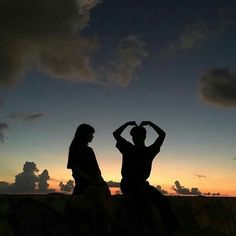 two people sitting on a rock at sunset