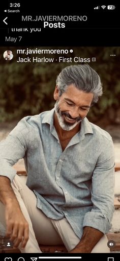 an older man with grey hair and beard sitting on a bench looking at his cell phone