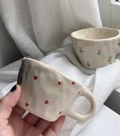 a hand holding a coffee cup with hearts on it and another mug in the background