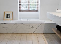 a bathroom with a marble bathtub and wooden floors in front of a white window