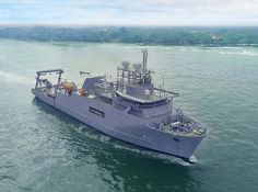 an aerial view of a navy ship sailing in the water with trees in the background