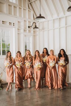 a group of women standing next to each other in front of a white wall holding bouquets