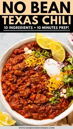 a white bowl filled with chili and topped with sour cream, cilantro, lime wedges and shredded cheese