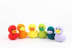 crocheted rubber ducks lined up in a row on a white background, with one yellow duck standing out from the others