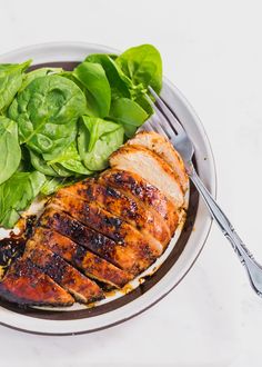 a white plate topped with meat and greens next to a fork on top of a table